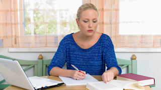 Eine Frau sitzt mit Bchern und Laptop am Schreibtisch.