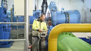 Ein Mitarbeiter kontrolliert technische Anlagen in einem Wasserwerk mit groen blauen Rohren und Ventilen.